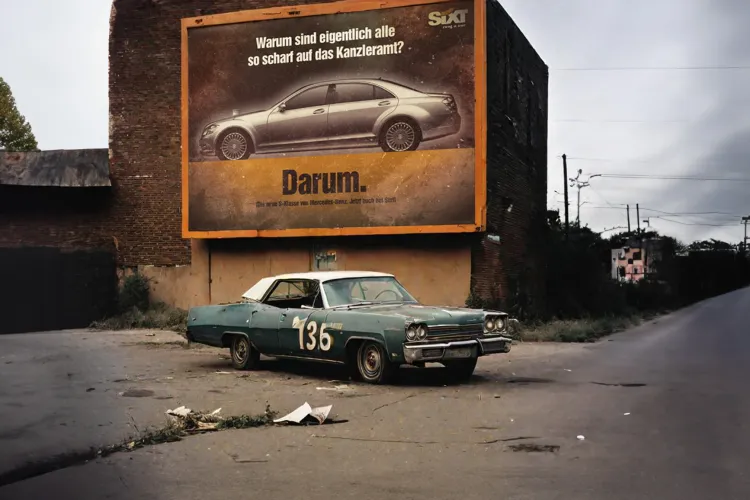 Altes Auto vor einer veralteten Plakatwand auf einer leeren Straße