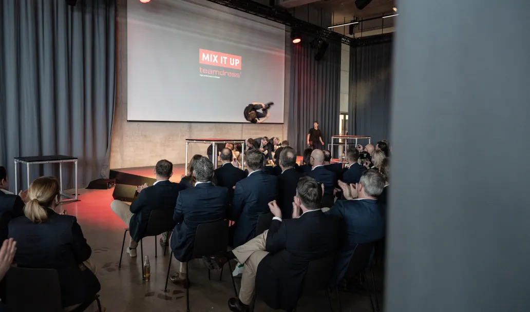 Ein Mann macht ein Salto &uuml;ber mehrere Personen vor dem teamdress logo