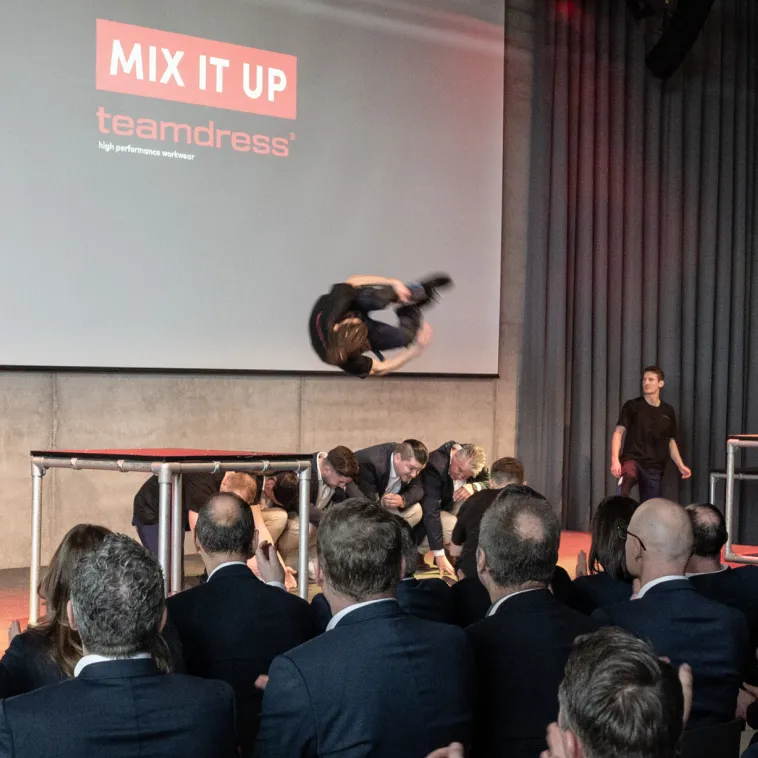 Mann macht Salto &uuml;ber eine Gruppe von Maennern